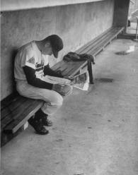 Baseball player Billy Joe Davidson sitting alone in the dugout reading a newspaper before a game